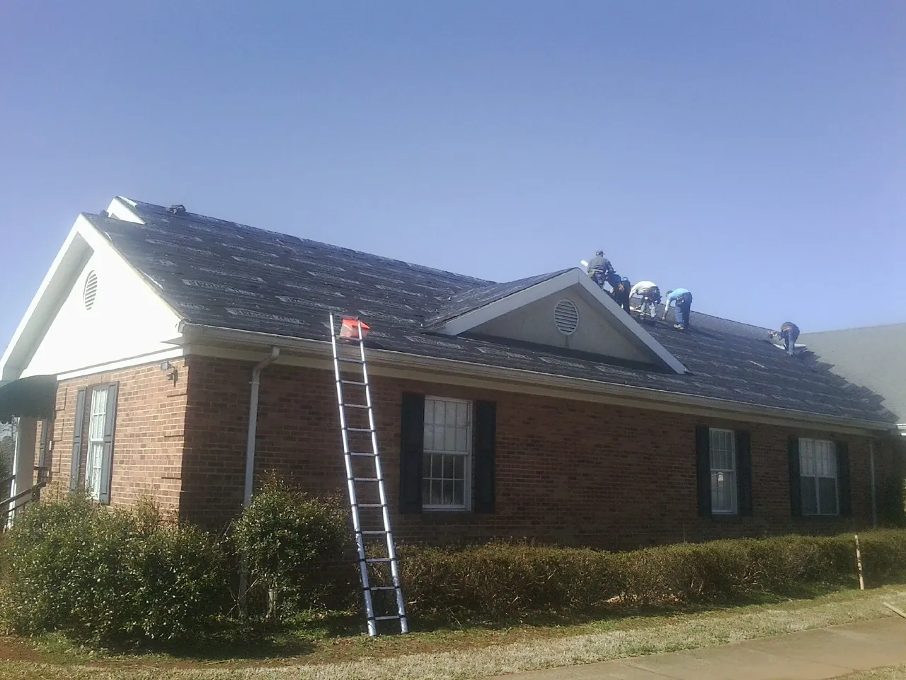 Crew tearing shingles off a brick ranch roof with a ladder set — Emergency Roof Repair work by our crew in Hopewell